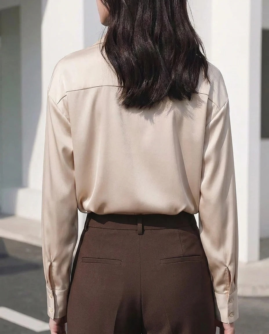 Woman wearing a champagne satin long sleeve blouse and brown high-waisted trousers.