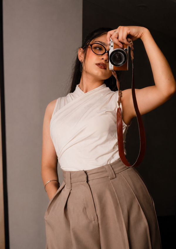 Woman in white halter top and beige pleated trousers holding a vintage camera.