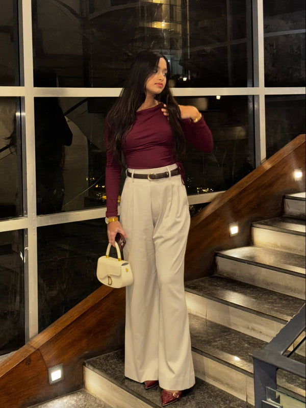 Woman in maroon long sleeve top and beige wide leg trousers standing on stairs