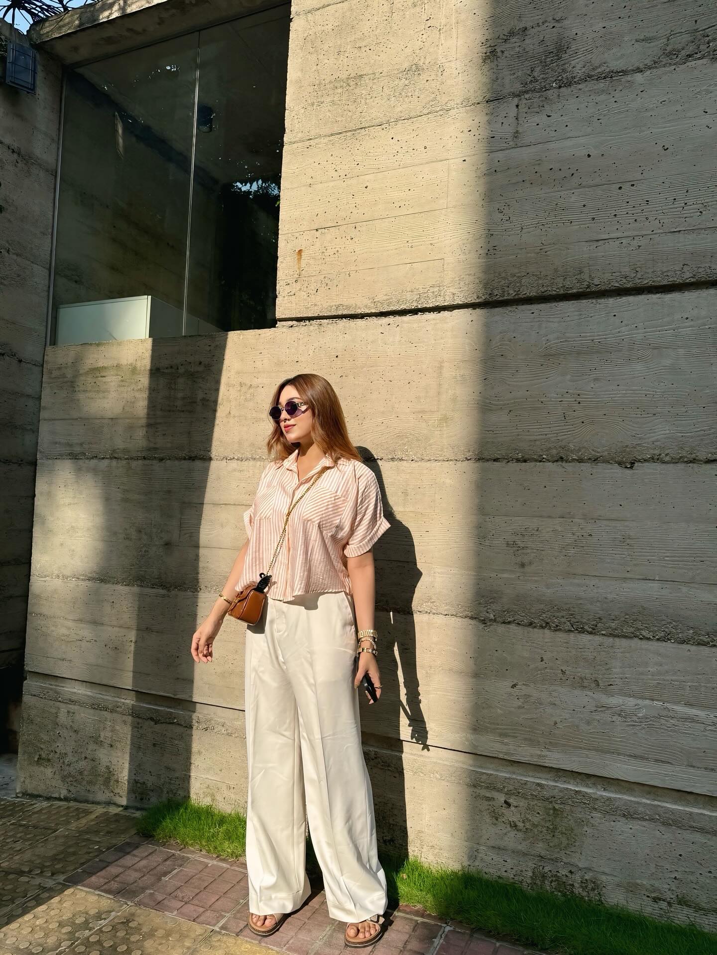 Woman in striped short sleeve shirt and white wide leg trousers posing outdoors.