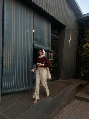 Woman in maroon long sleeve top and beige wide-leg trousers walking outdoors.