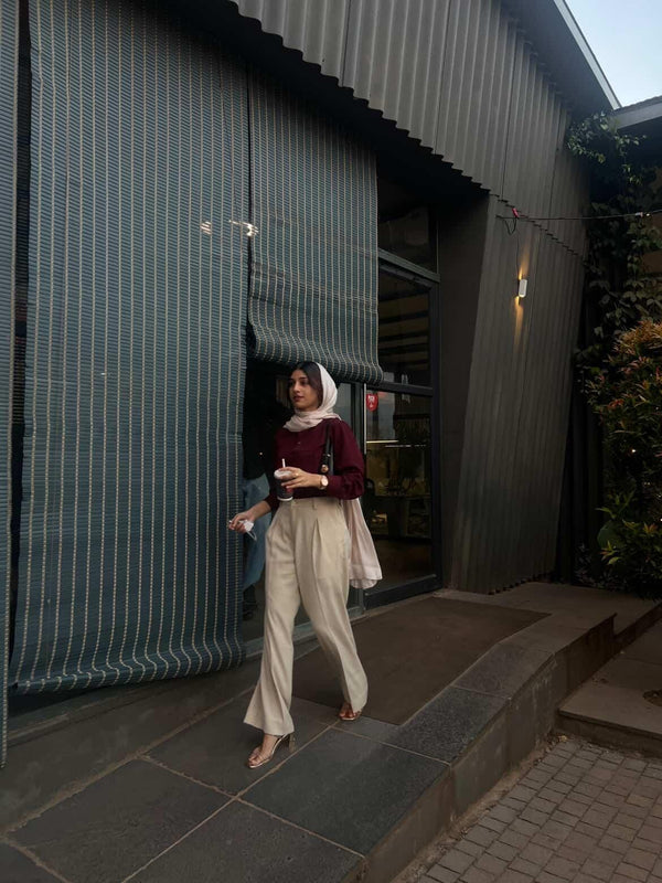 Woman in maroon long sleeve top and beige wide-leg trousers walking outdoors.
