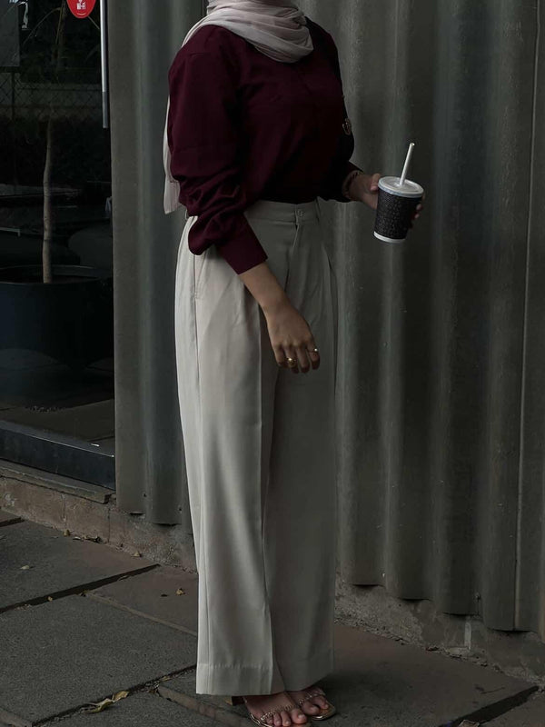 Woman in maroon long sleeve top and cream wide-leg trousers holding a drink.