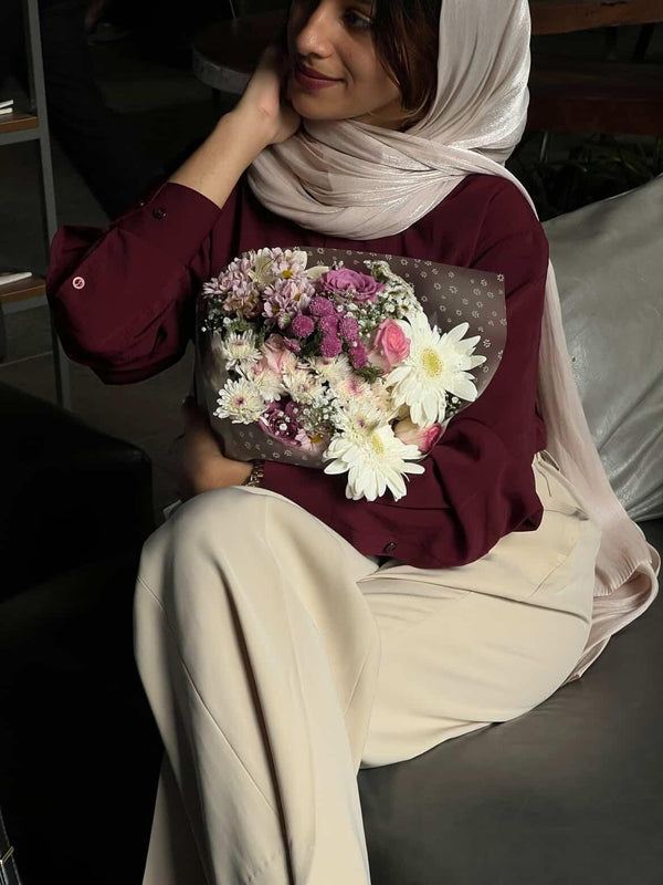 Woman in maroon blouse and beige trousers holding a colorful flower bouquet.