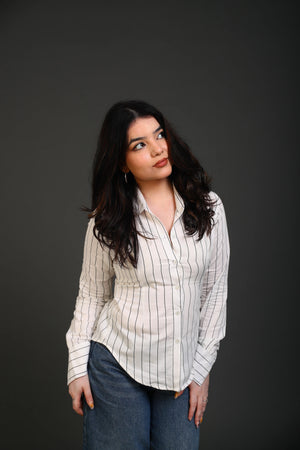 Woman wearing a white striped button-down shirt and blue denim jeans.