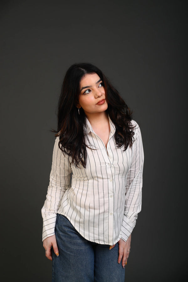 Woman wearing a white striped button-down shirt and blue denim jeans.