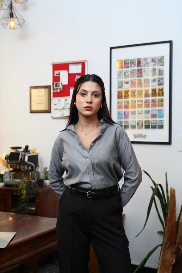 Young woman wearing a grey button-down shirt and black trousers in a modern office setting.
