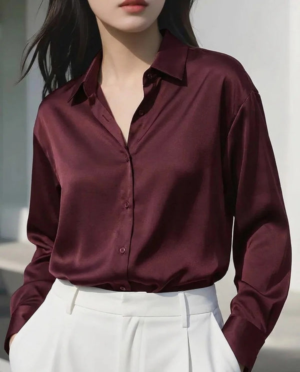 Woman wearing a maroon satin long sleeve button-down shirt and white trousers.