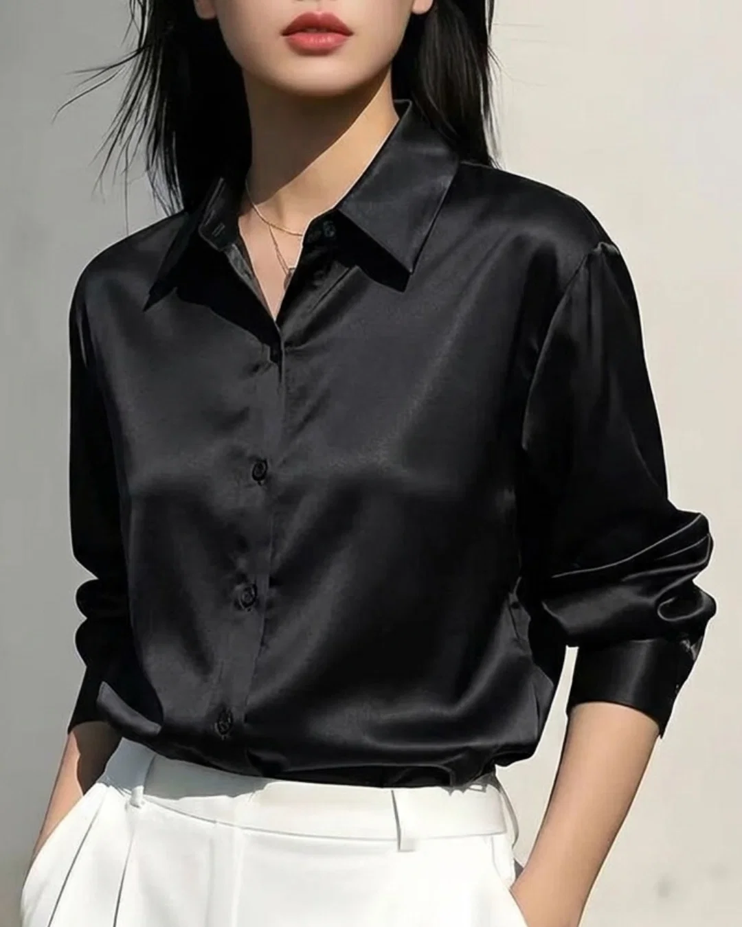 Woman wearing a black satin long sleeve button-down shirt and white trousers.