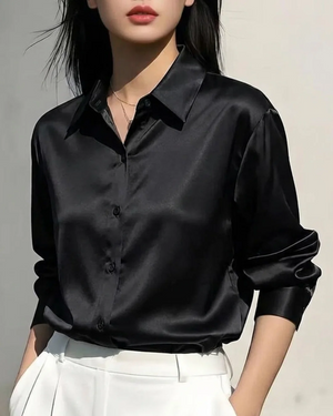 Woman wearing a black satin long sleeve button-down shirt and white trousers.