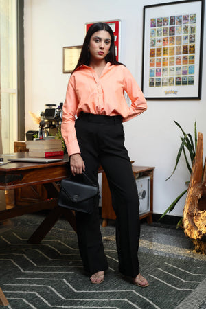 Woman wearing a peach long-sleeve button-down shirt and black wide-leg trousers holding a handbag.