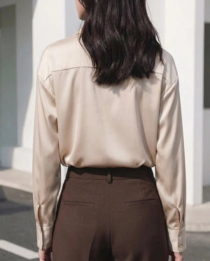 Woman wearing a champagne satin long sleeve blouse and brown high-waisted trousers.