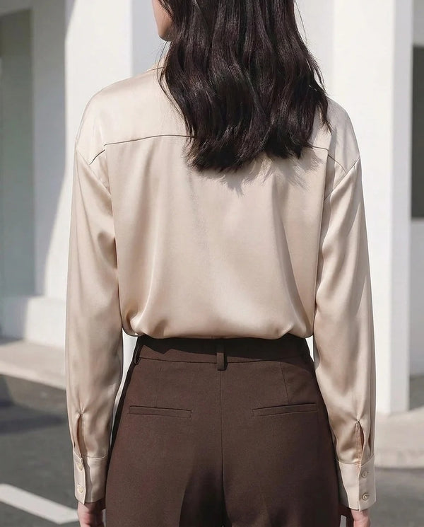 Woman wearing a champagne satin long sleeve blouse and brown high-waisted trousers.