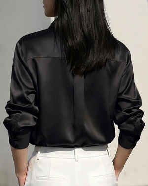 Woman wearing a black satin long sleeve button-down shirt and white trousers.
