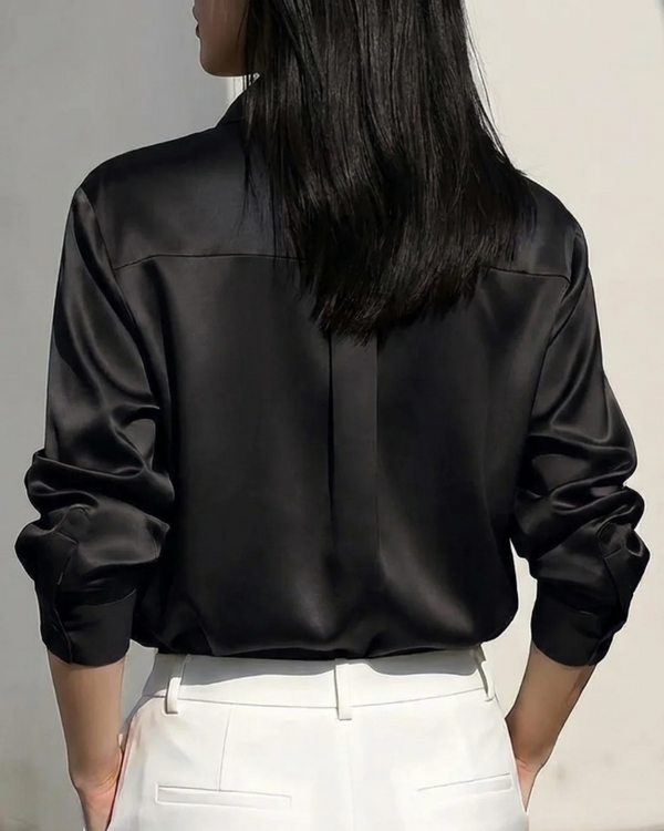 Woman wearing a black satin long sleeve button-down shirt and white trousers.