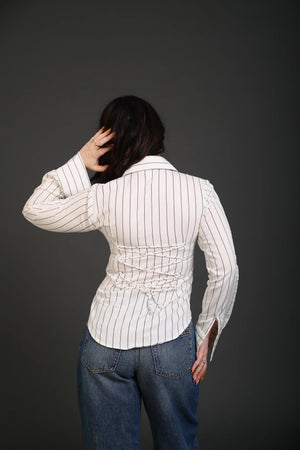 Back view of a woman wearing a white striped corset-style shirt and blue denim jeans.