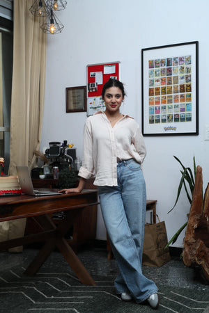 Woman in a white linen shirt and light blue wide-leg jeans posing in a home office.