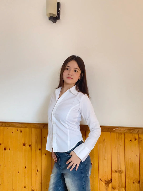 Woman wearing a white long sleeve button-down shirt and blue denim jeans.