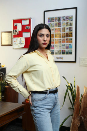 Woman wearing a pale yellow button-down shirt and light wash denim jeans.
