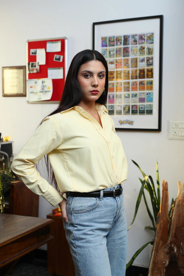 Woman wearing a pale yellow button-down shirt and light wash denim jeans.