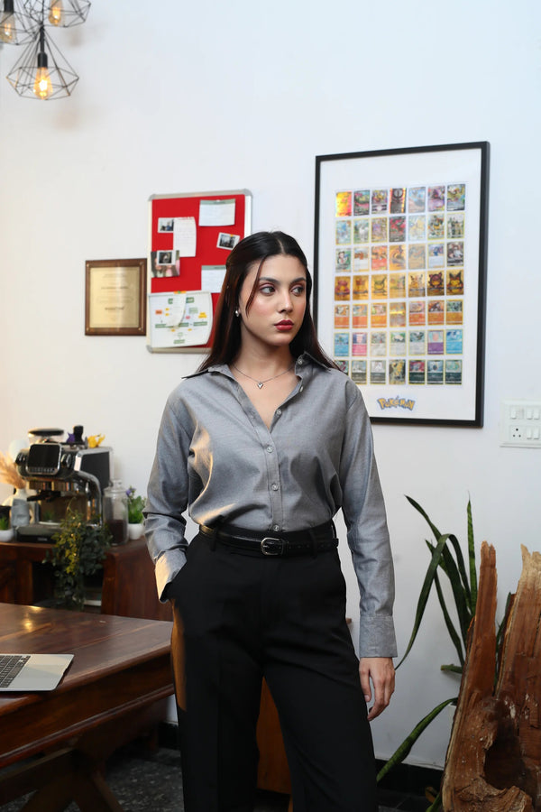 Woman wearing a grey long sleeve button-down shirt and black trousers in a modern office setting.