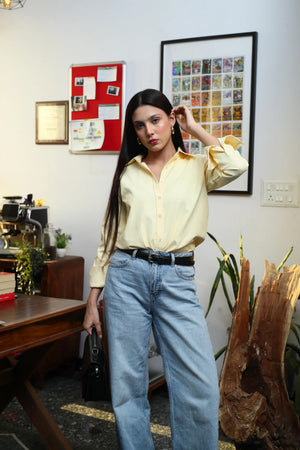 Woman in yellow button-down shirt and light blue wide-leg jeans standing indoors.